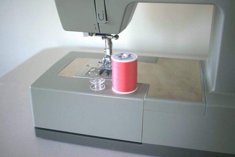 coral thread spool and empty bobbin sitting on sewing machine