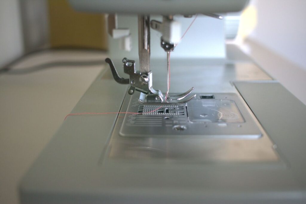 sewing machine pressure foot with thread going through needle and laying at the back on the sewing machine