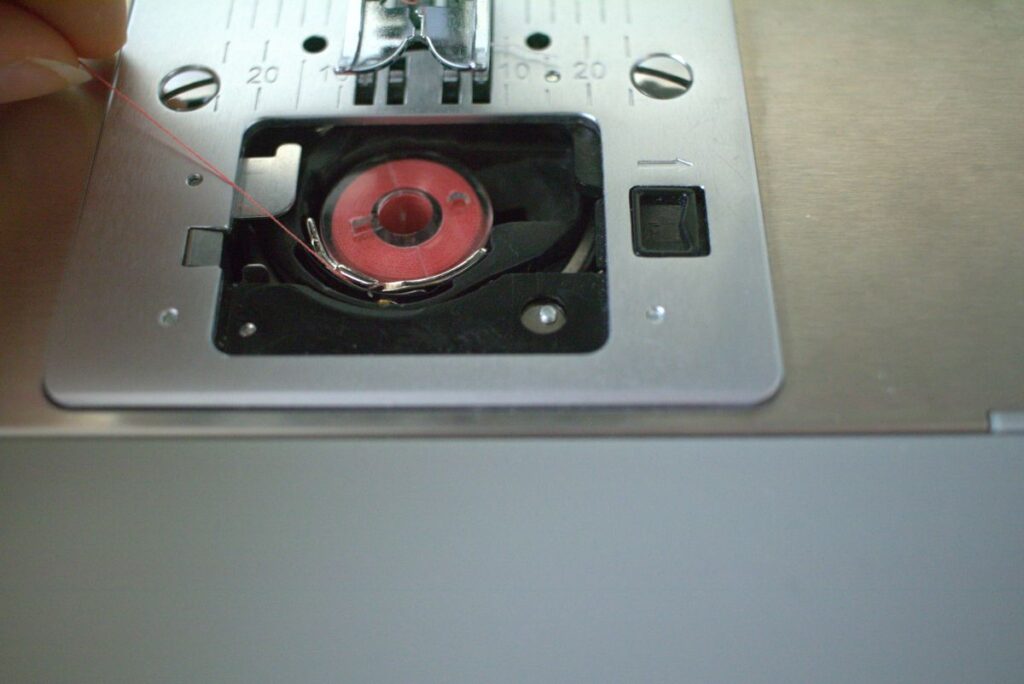 hand pulling thread from bobbin into notch in bobbin case