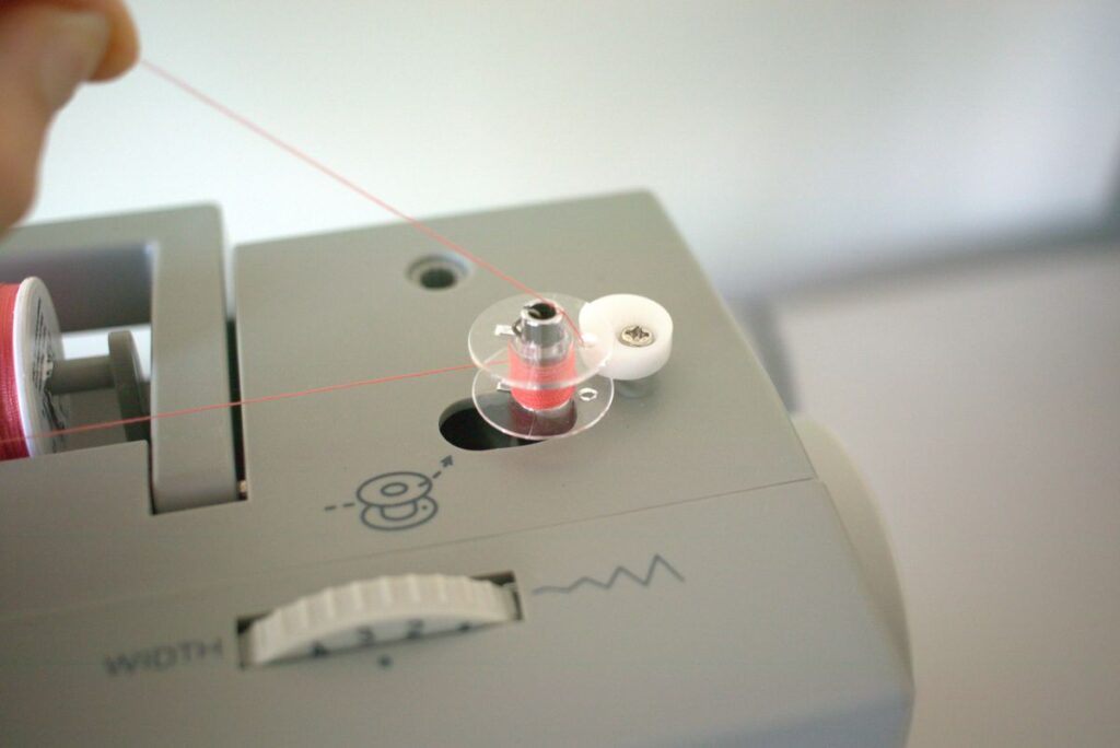 thread winding onto bobbin with hand holding thread coming from top of the bobbin 