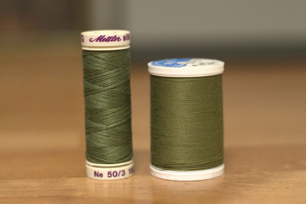 two spools of green thread with different winds sitting on table