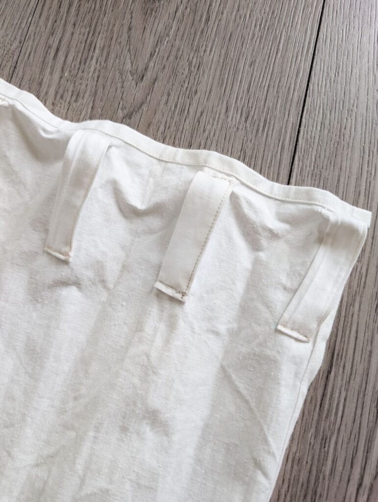 top corner of white diy curtain laying flat with back tabs facing up