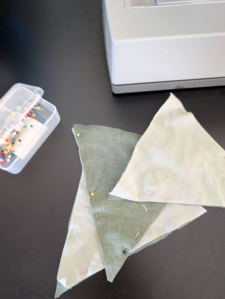 fabric triangles for diy bunting garland on table next to needles and sewing machine